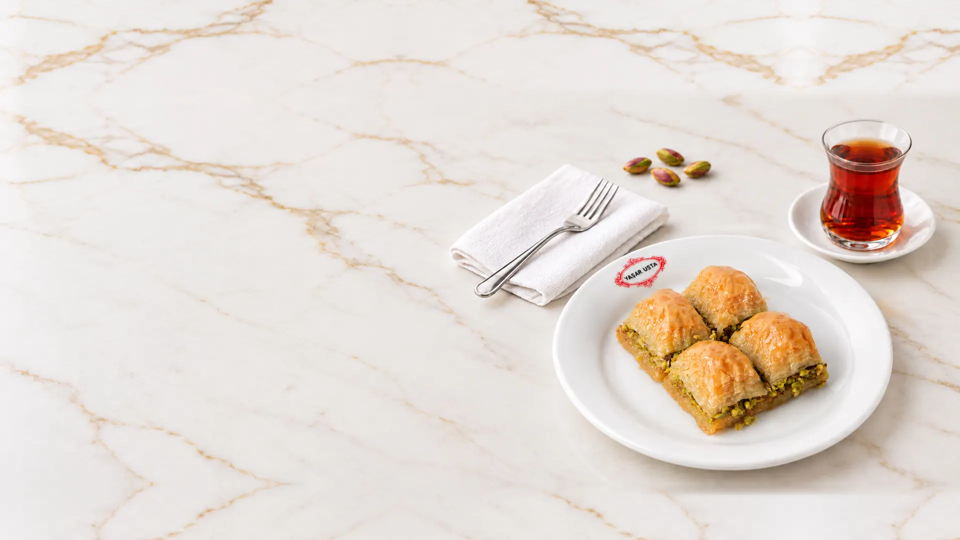 Yaşar Usta tabağında dört dilim fıstıklı baklava, yanında çay ve fıstık