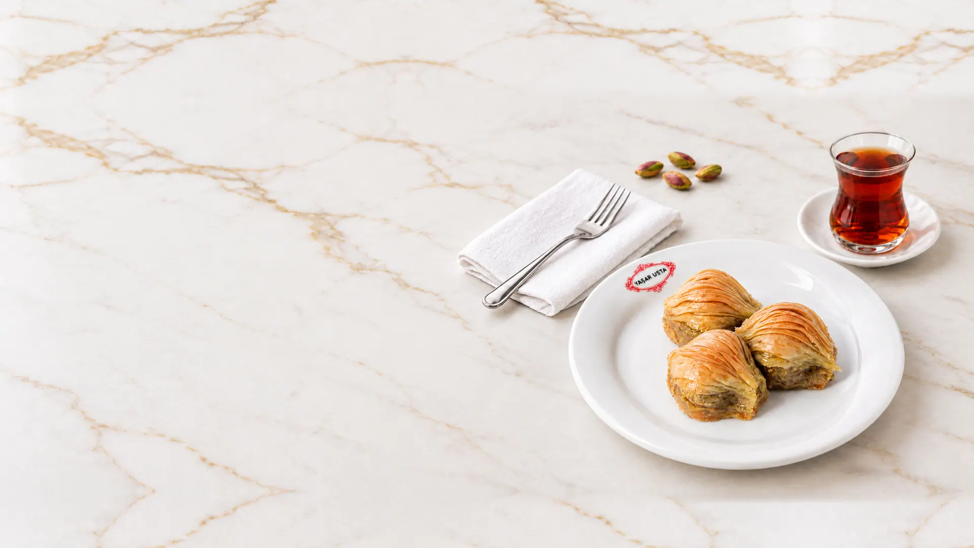 Yaşar Usta tabağında üç midye baklava, yanında çay ve fıstık