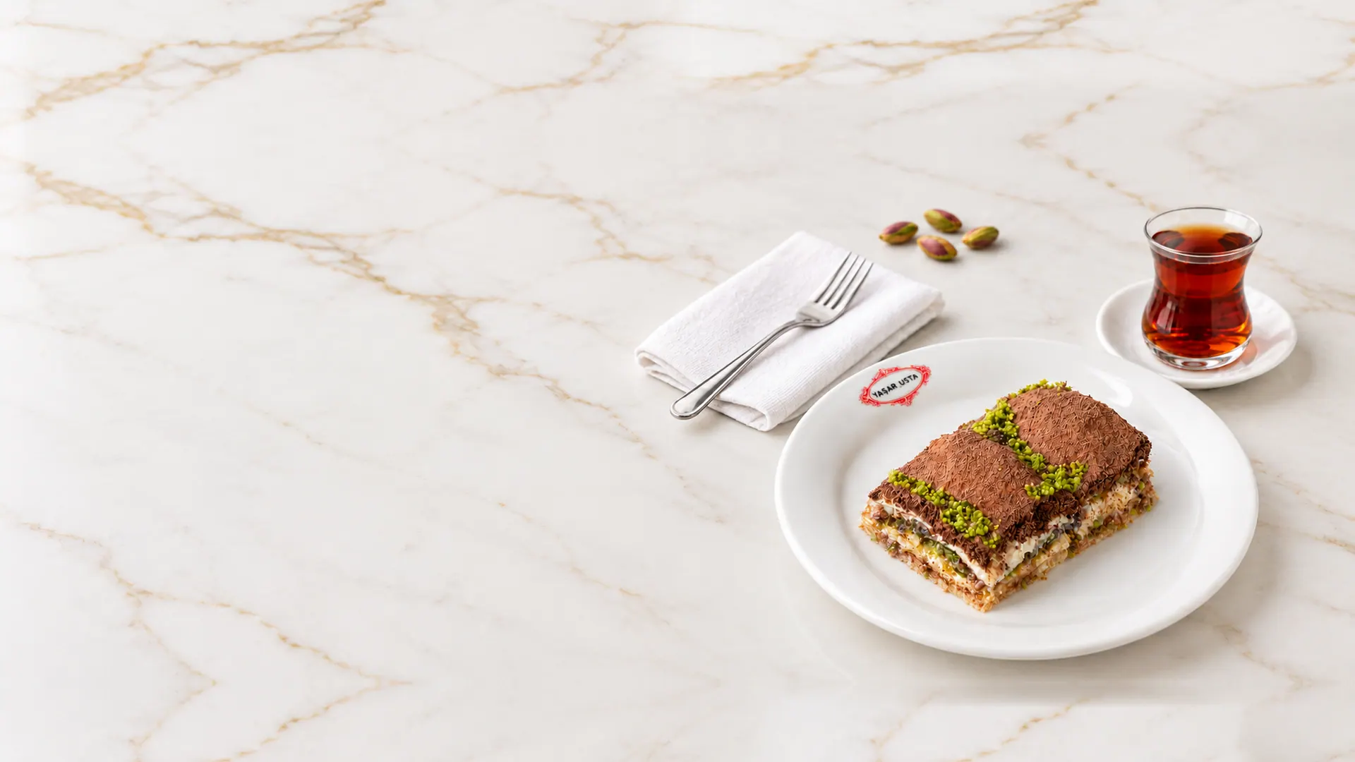 Yaşar Usta tabağında Soğuk Baklava, yanında çay ve Antep fıstığı, mermer masada